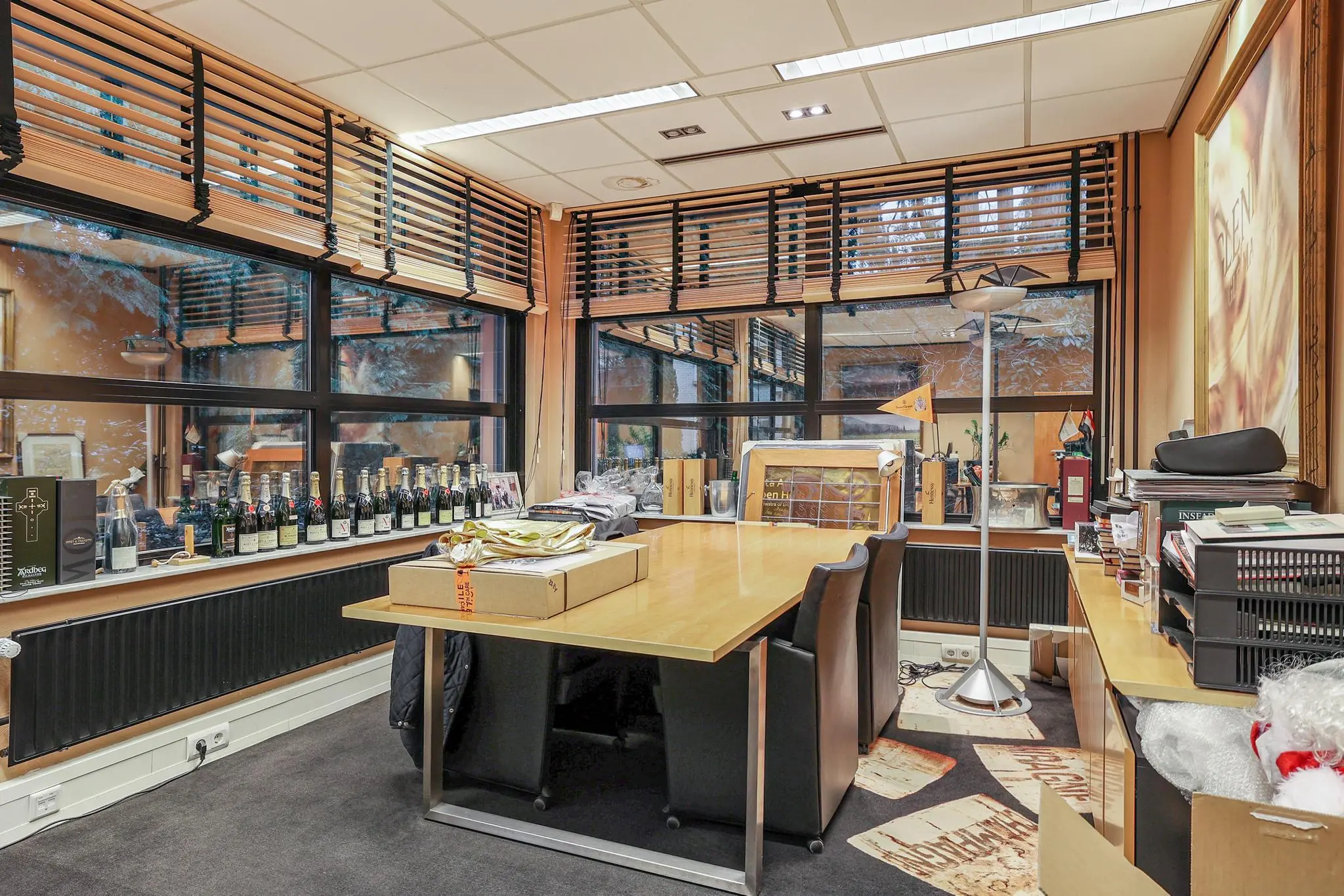 Moderne kantoorruimte aan de Oude Utrechtseweg met een grote vergadertafel, flessen drank op de vensterbank en houten jaloezieën voor de ramen.